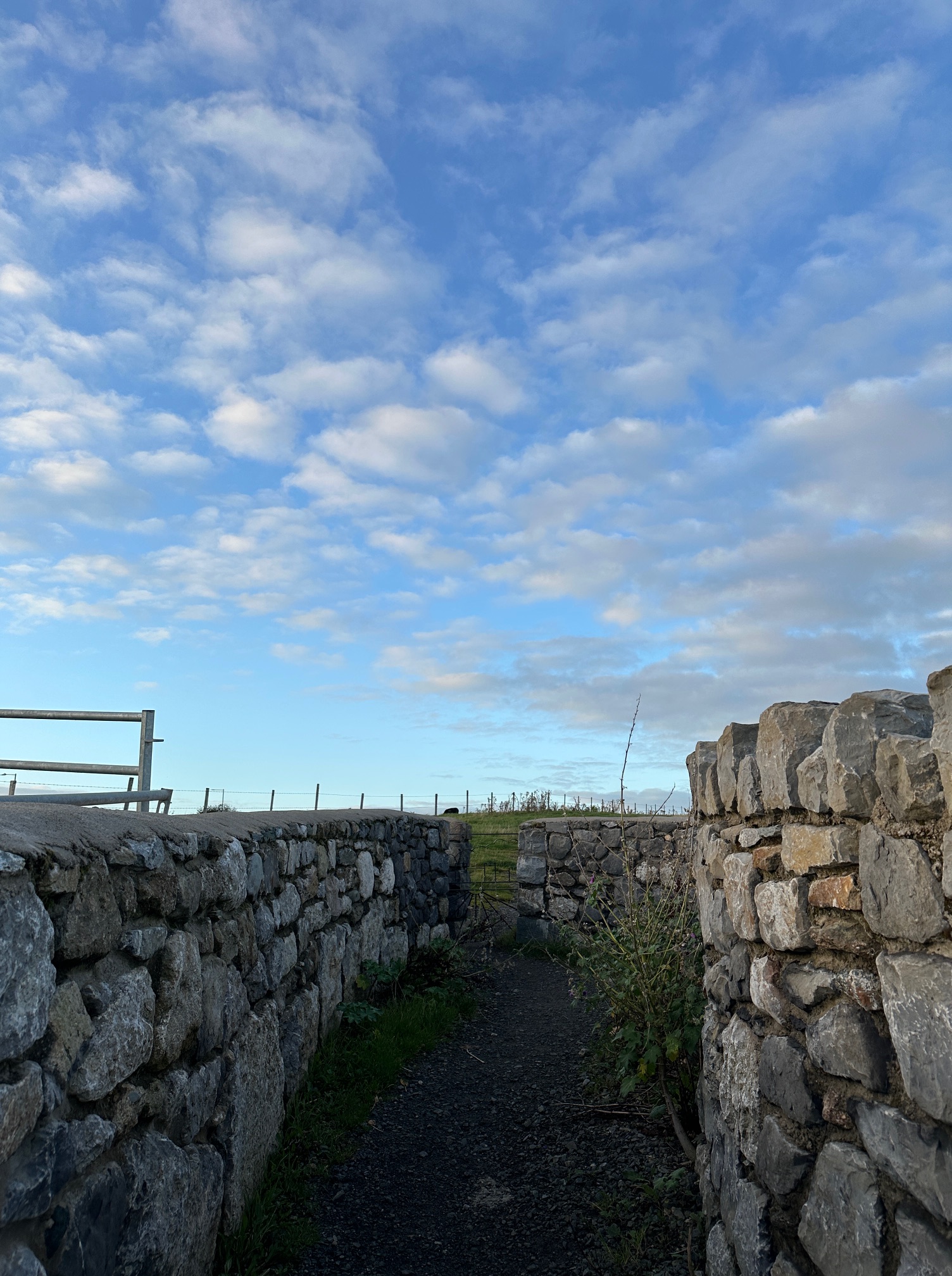 blue sky with scattered clouds and ancient rock wall leading to path